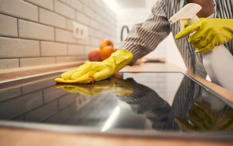 Clean kitchen countertop being wiped with yellow gloves and spray bottle.