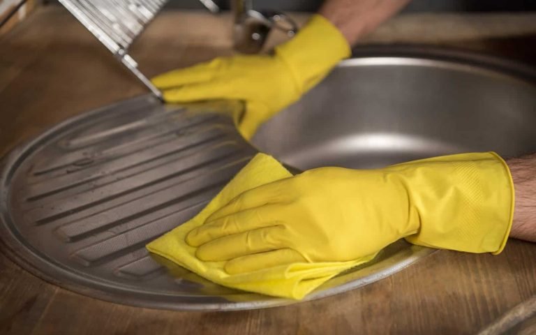 Image of a professional cleaning a stainless steel kitchen sink with a yellow glove, showcasing expert services.