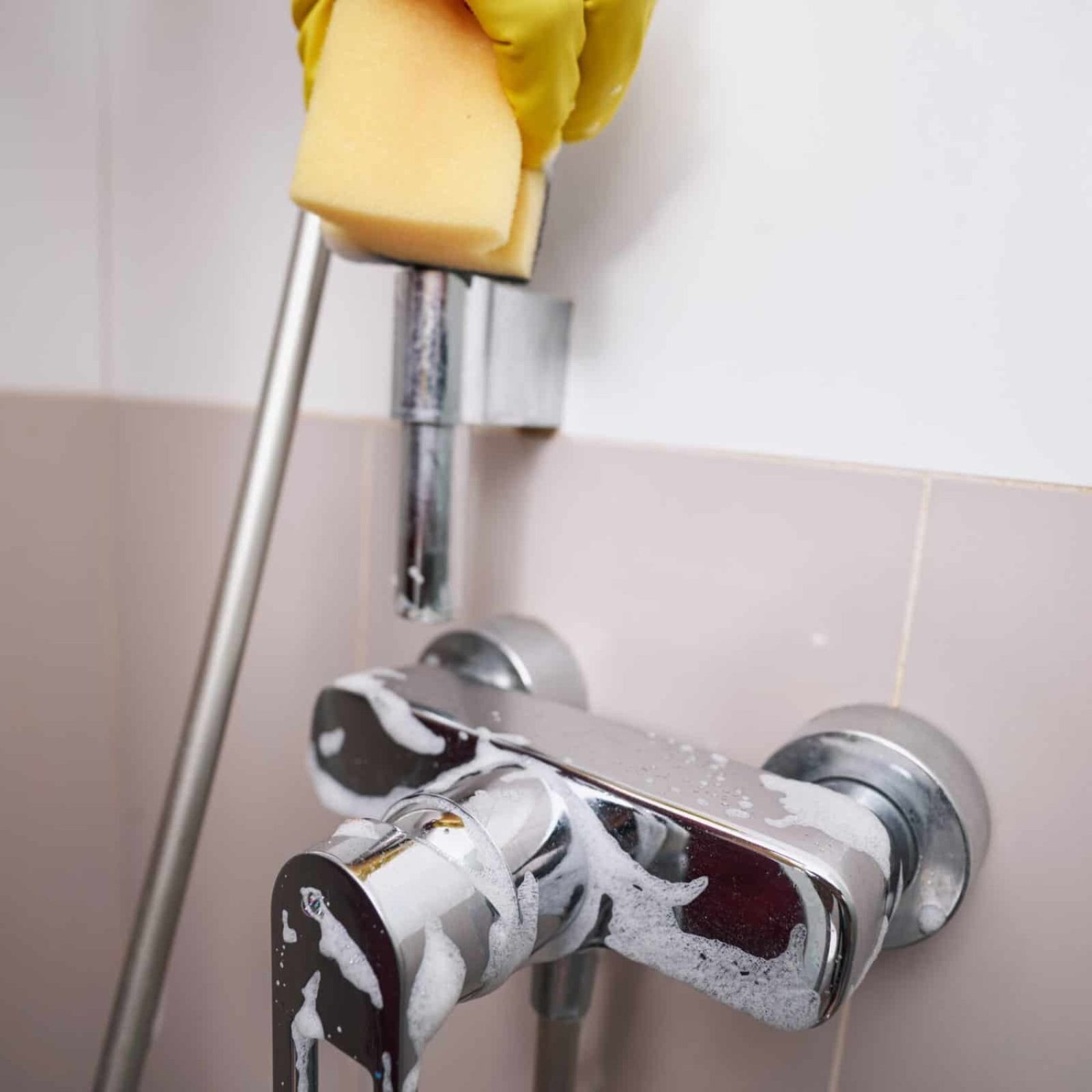 ALT Text: Hand in yellow glove scrubbing bathroom faucet with sponge for deep cleaning.