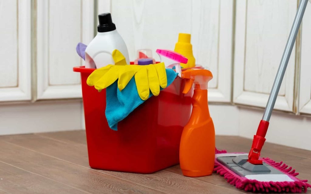 Cleaning supplies in a red bucket with gloves, spray bottles, and cleaning tools.